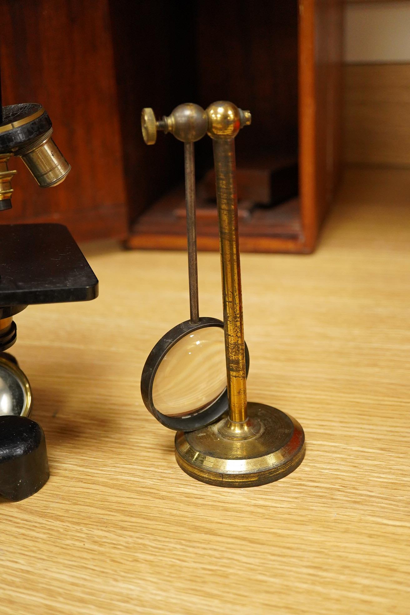 An early 20th century pine and plywood cased microscope by C.Baker, London, containing an integral drawer with alternative lenses, and a magnifying glass on a brass stand, the case dimensions; 38cm high, 18cm wide, 27.5c